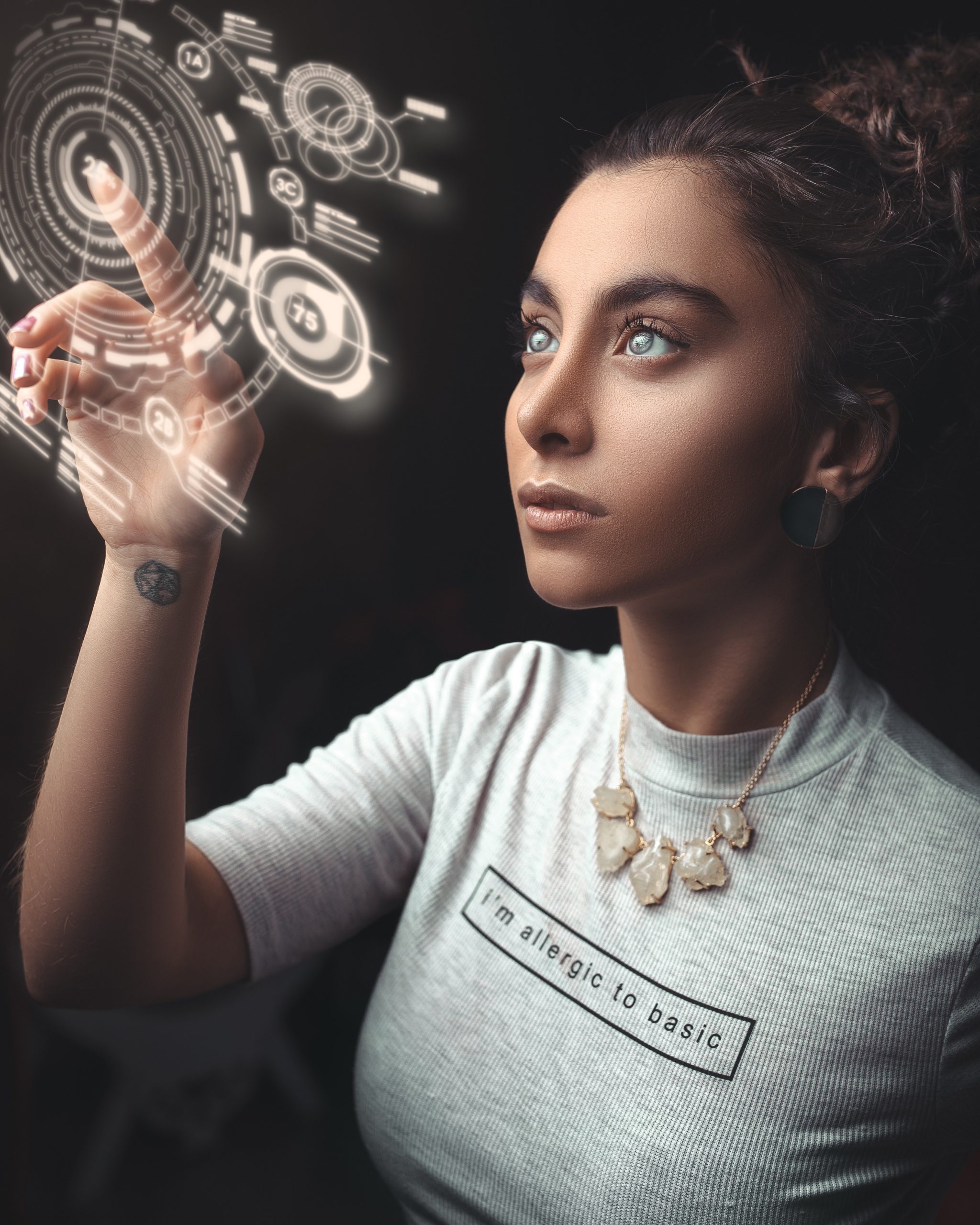 A young woman in a t-shirt uses her fingertip to interact with a hologram if a digital diagram against a blackened background